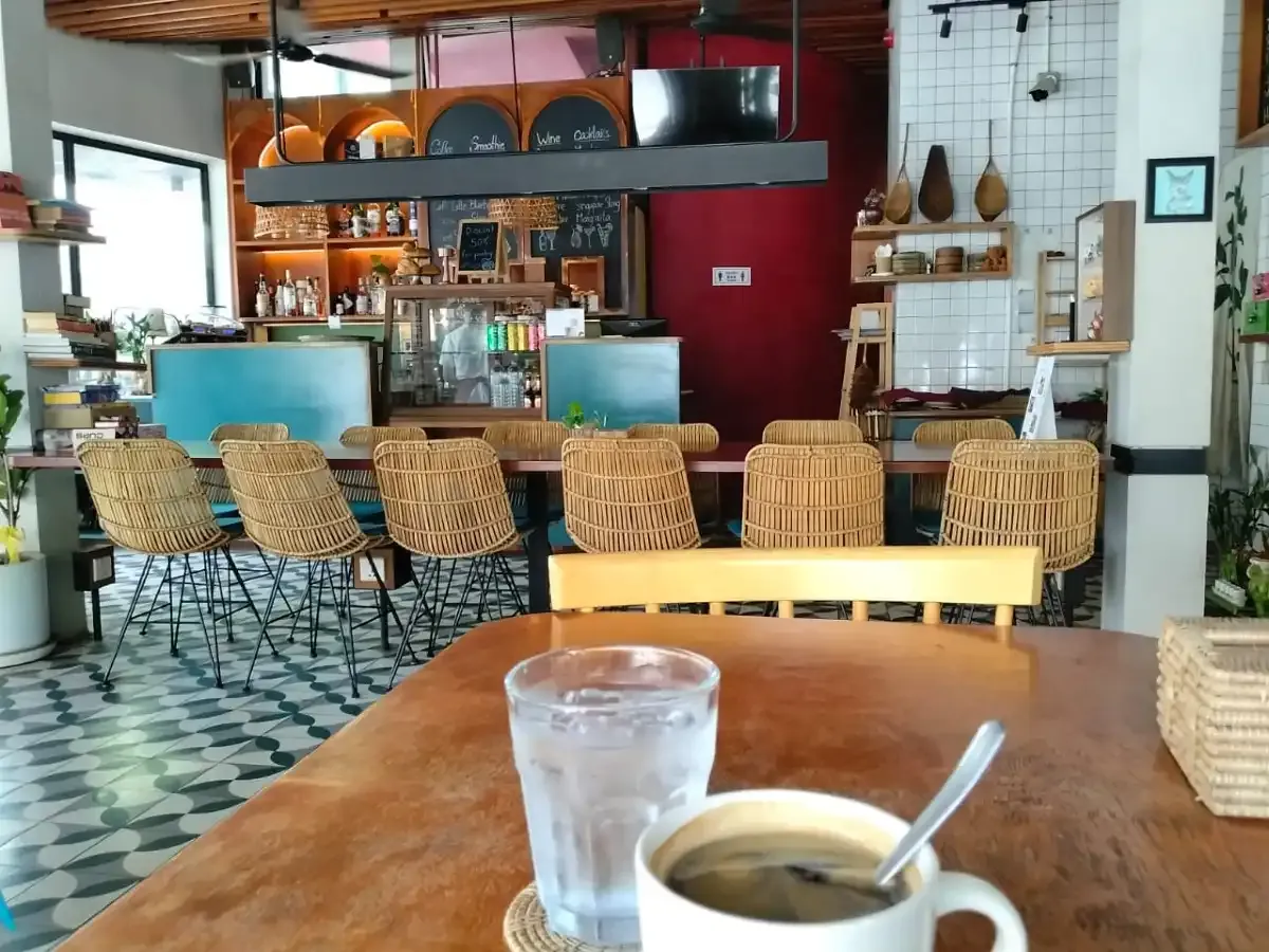 Dining room of Amun Bar & Restaurant, with rattan bar stools and an americano on a table in the foreground