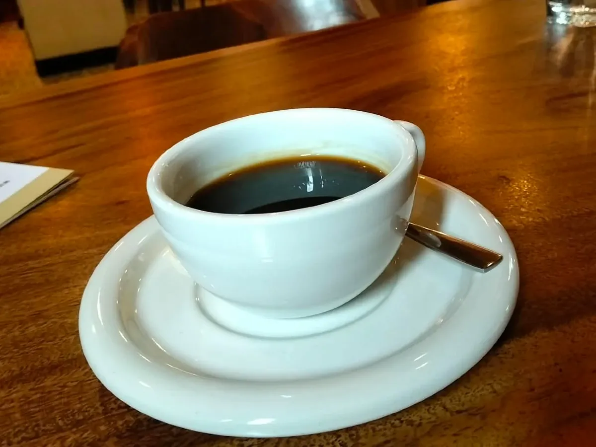 Americano in a white cup and saucer on a wooden table at The Source Café